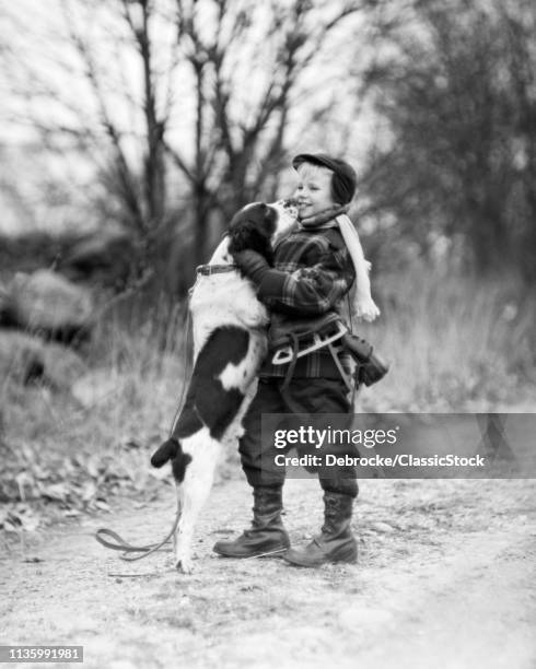 1950s SMILING BOY WEARING WINTER COAT HAT SCARF BOOTS ICE SKATES SLUNG OVER SHOULDER HUGGING ENGLISH SPRINGER SPANIEL DOG