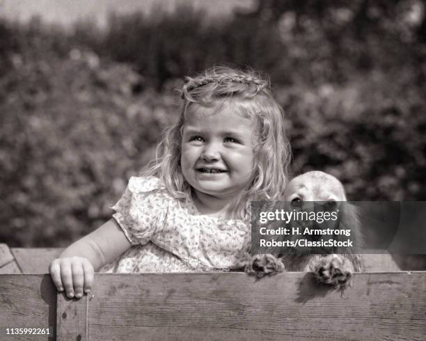 1930s PRETTY SMILING BLOND YOUNG GIRL IN WOODEN WAGON WITH COCKER SPANIEL PUPPY LOOKING AT CAMERA
