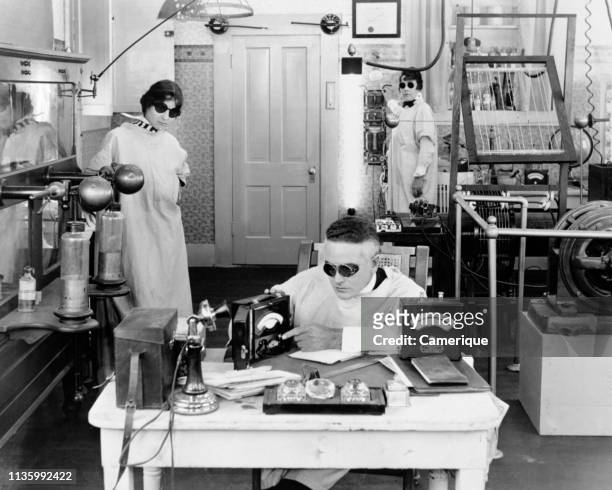 1920s THREE MAD SCIENTISTS WORKING EXPERIMENTING INVENTING IN ELECTRONICS LABORATORY ALL WEARING DARK GOGGLES & WHITE LAB COATS