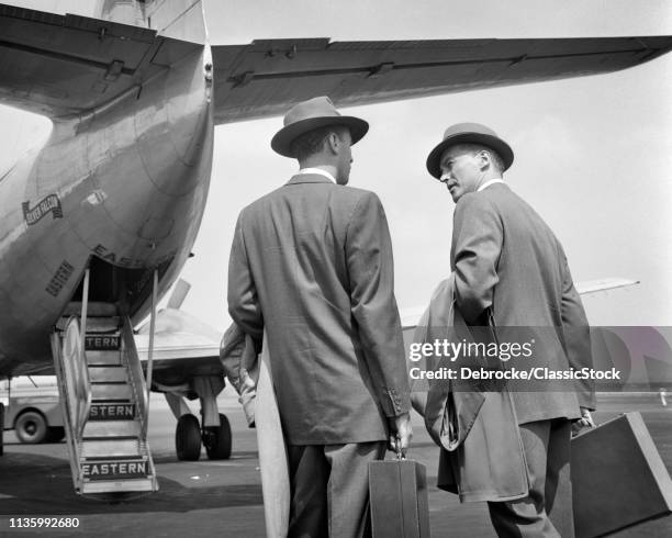 1950s TWO BUSINESSMEN TALKING ON TARMAC ABOUT TO ENTER REAR DOORS OF EASTERN AIRLINES PASSENGER PLANE