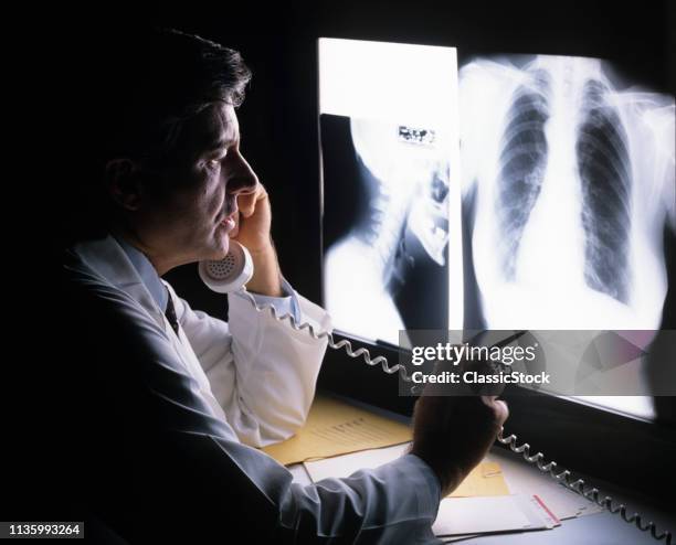 1980s MAN DOCTOR READING X-RAY SPEAKING ON TELEPHONE