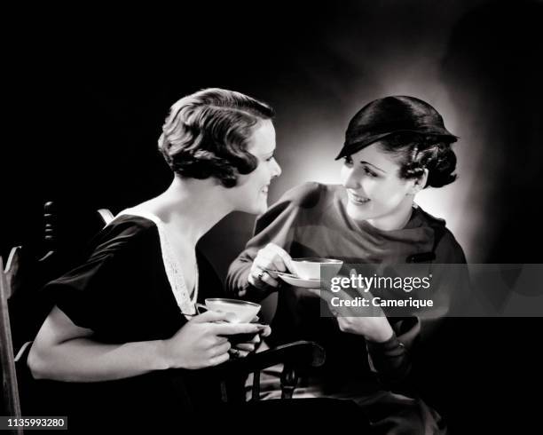 1930s TWO SMILING WOMEN SITTING TOGETHER DRINKING TEA TALKING AND GOSSIPING