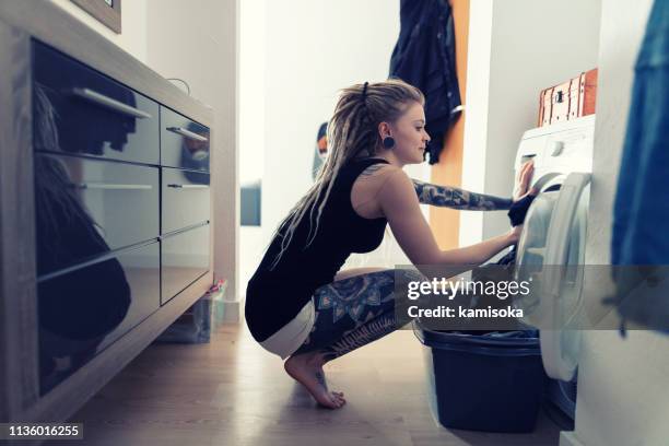 tätowierte junge frau wäscht ihre wäsche zu hause - hipster in a kitchen stock-fotos und bilder