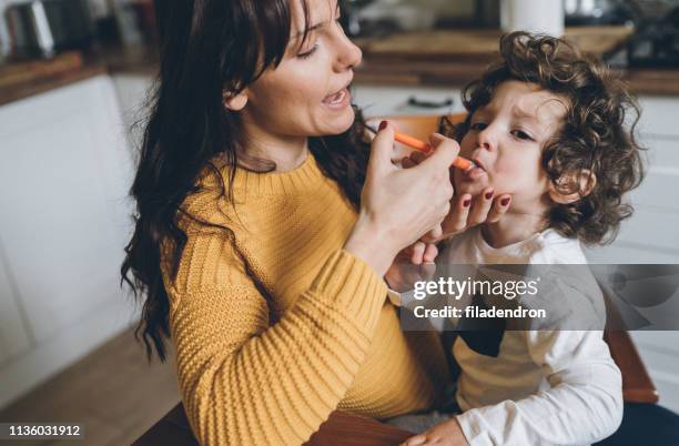 mother giving syrup to her son - hand over mouth stock pictures, royalty-free photos & images