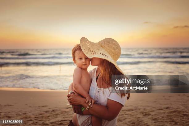 moeder met zoon genieten van zonsondergang op het strand - zonnehoed stockfoto's en -beelden