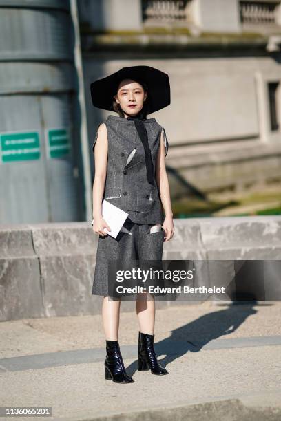 Guest wears a black hat, a white stitched grey sleeveless top, a grey skirt, shiny separated end black boots, outside Maison Margiela, during Paris...
