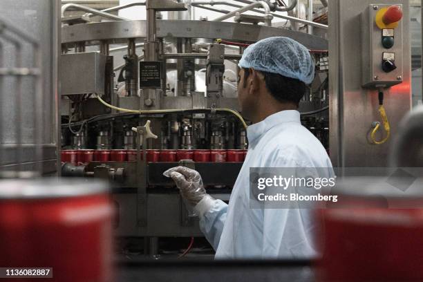 An employee monitors cans being filled with Coca-Cola Co. Brand Coke carbonated soft drink at the Moon Beverages Ltd. Coca-Cola Happiness Factory in...
