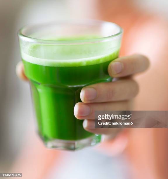 hand of woman holding a glass of green smoothie - wheatgrass stock pictures, royalty-free photos & images
