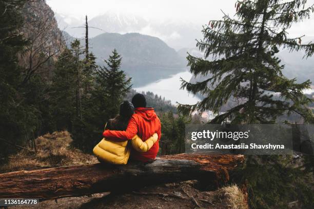 frau und mann sitzen im wald und umarmen und schauen auf die bayerische alpenlandschaft - couple forest stock-fotos und bilder