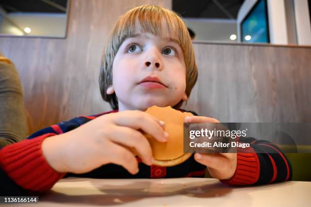 little boy eating a hamburger sitting at a restaurant table. view from a low angle - hand holding burger stock pictures, royalty-free photos & images