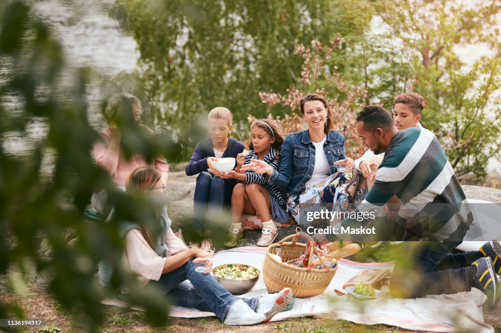 Happy family and friends having food on lakeshore in park
