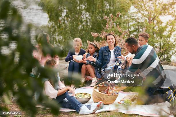 happy family and friends having food on lakeshore in park - family at a picnic ストックフォトと画像