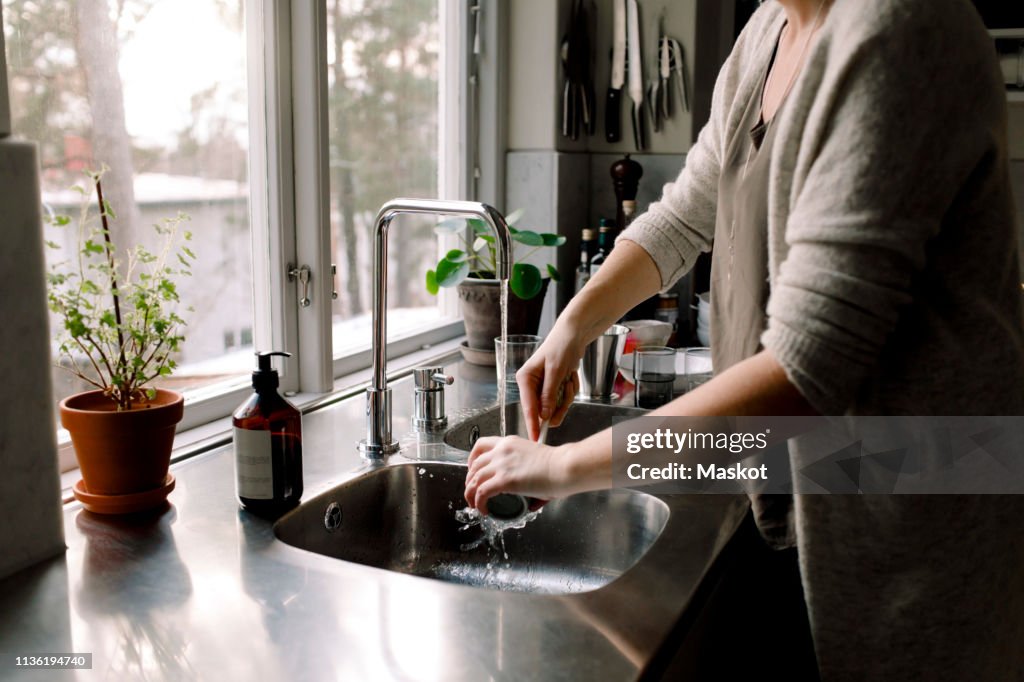 Midsection of woman cleaning cup in kitchen sink at home