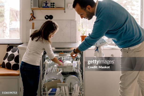 father and daughter arranging utensils in dishwasher at kitchen - domestic chores photos et images de collection