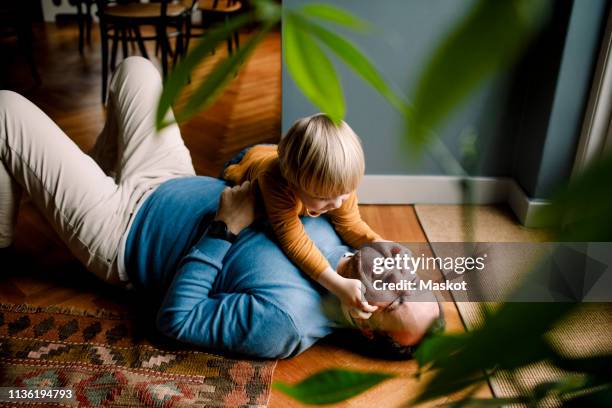 playful daughter pinching cheerful father's cheeks on floor at home - vita di famiglia foto e immagini stock