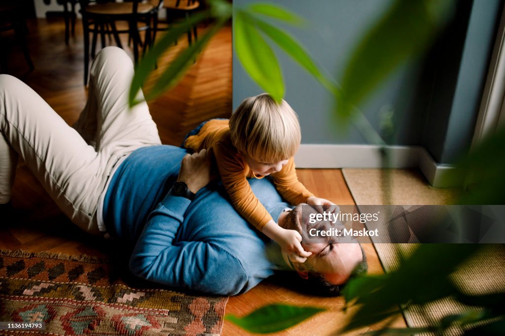 Playful daughter pinching cheerful father's cheeks on floor at home