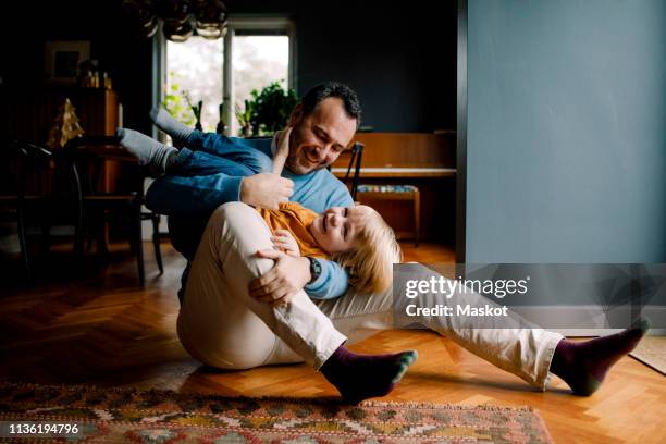 full length of happy playful father carrying daughter while sitting on hardwood floor at home - child sitting stock-fotos und bilder