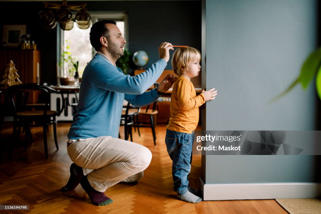 Full length of father measuring daughter's height against wall at home