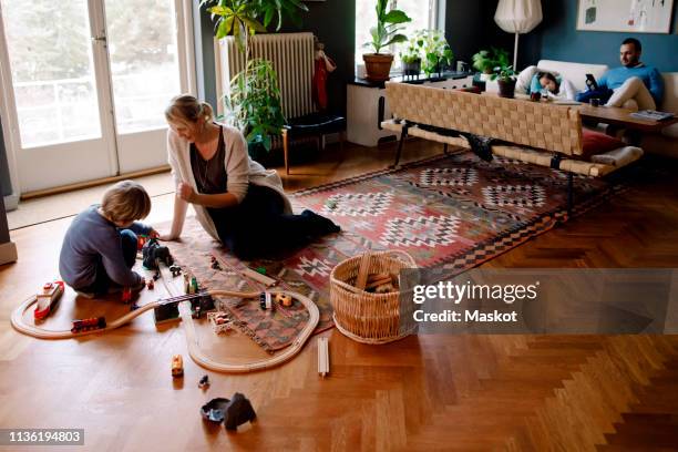 mother and daughter playing with train set in living room at home - small child sitting on floor stockfoto's en -beelden