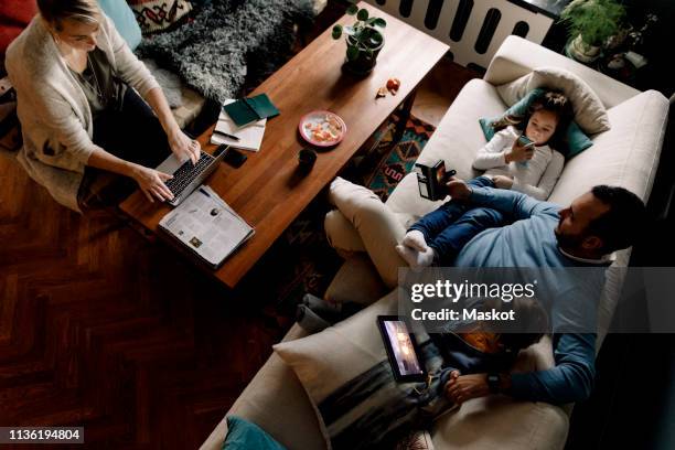 high angle view of family using various technologies in living room at home - family ipad stockfoto's en -beelden