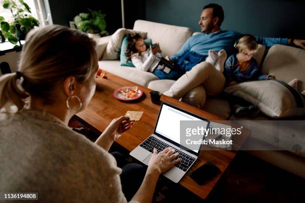mother online shopping while man and daughters using various technologies in living room - mature man using phone tablet stock pictures, royalty-free photos & images