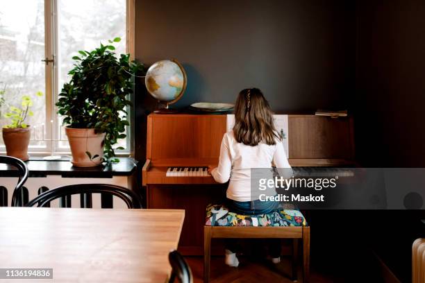 rear view of girl playing piano while sitting in living room at home - practicing piano stock pictures, royalty-free photos & images