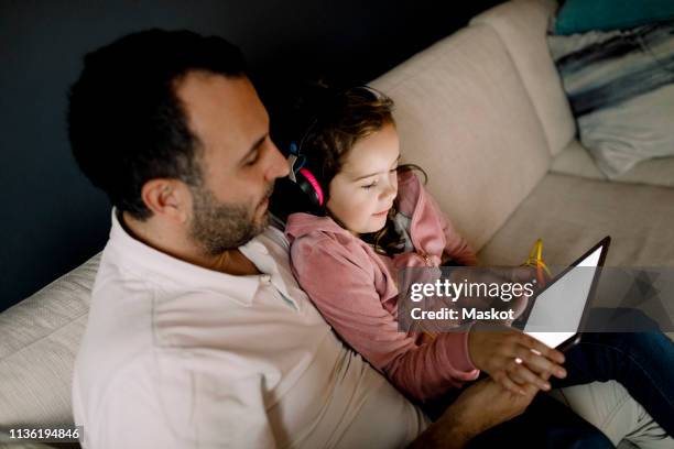 high angle view of father assisting daughter in using digital tablet on couch at home - parental control stock-fotos und bilder