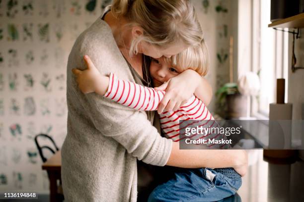 loving daughter embracing mother while sitting on kitchen counter at home - nageslacht stockfoto's en -beelden