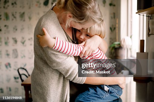 Loving daughter embracing mother while sitting on kitchen counter at home Loving daughter embracing mother while sitting on kitchen counter at home