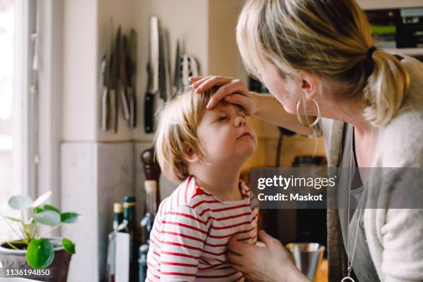 caring mother looking at daughter's bruised eye in kitchen - cardenal lesión física fotografías e imágenes de stock