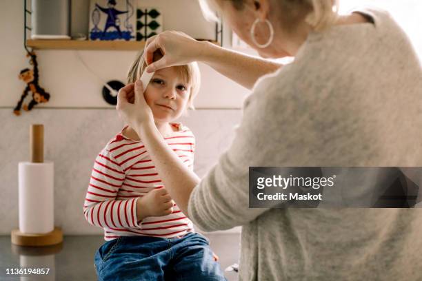 mother applying bandage on daughter's face at home - wounded stockfoto's en -beelden