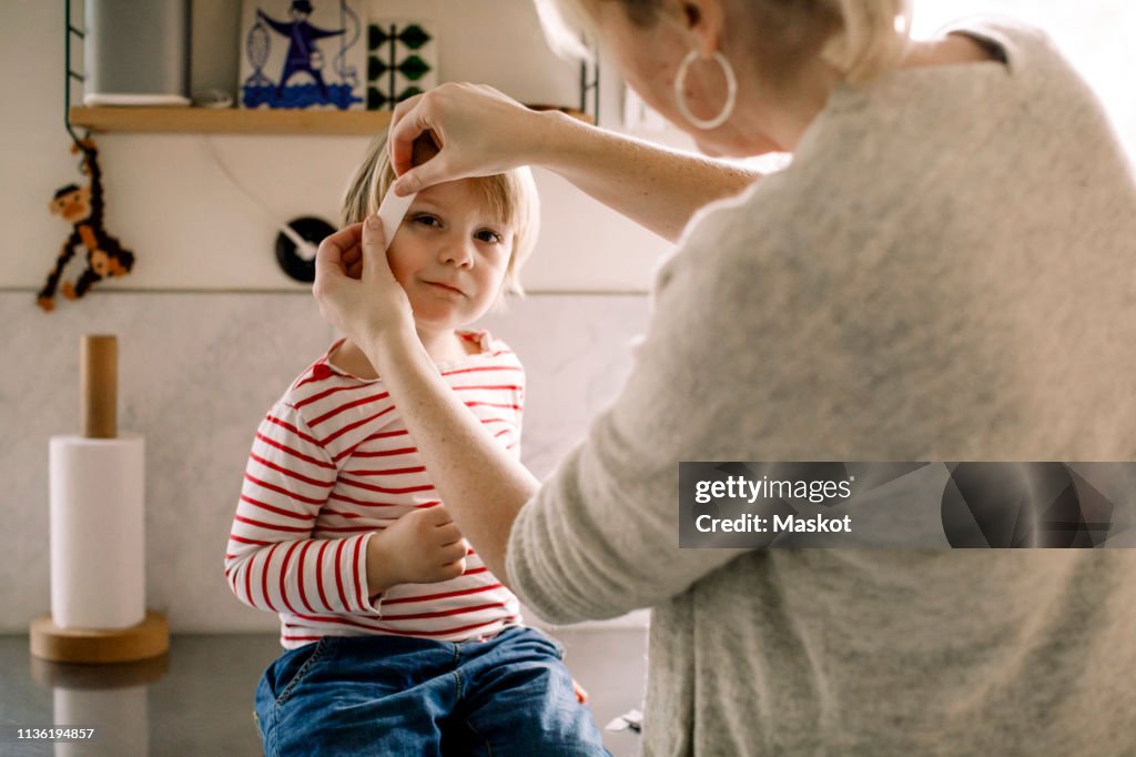 Mother applying bandage on daughter's face at home