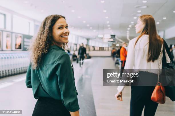 portrait of smiling businesswoman walking with female colleague at airport - business travel stock pictures, royalty-free photos & images