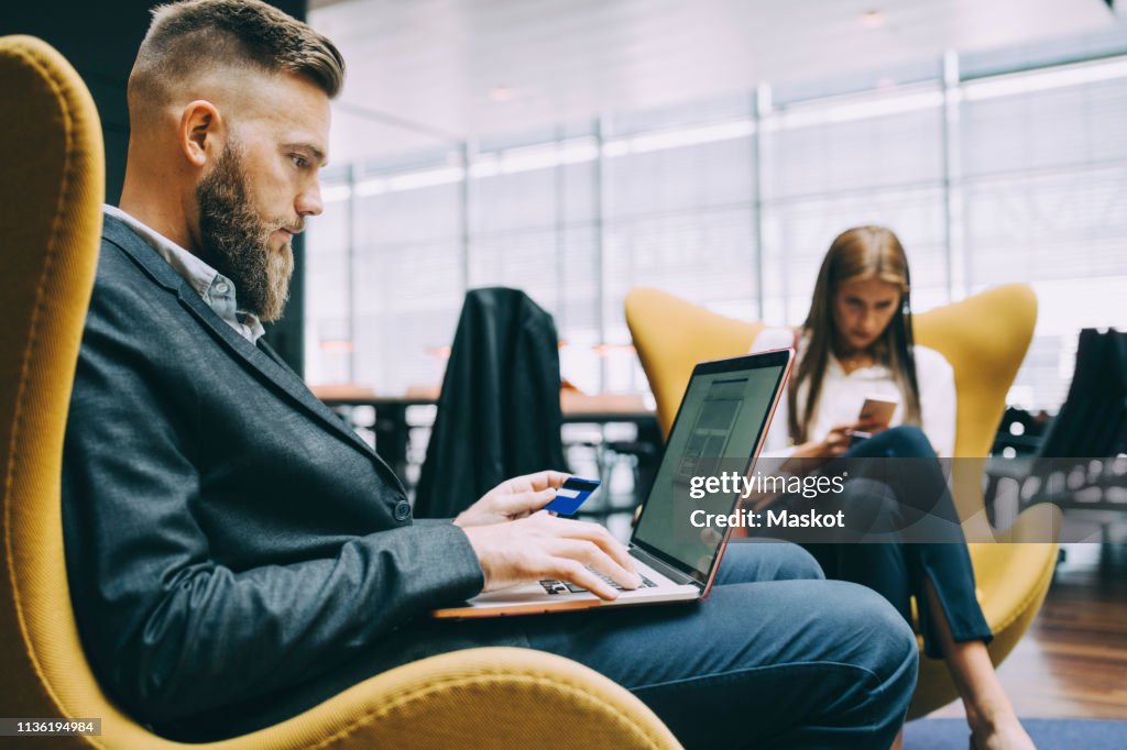 Side view of businessman holding credit card while using laptop at airport