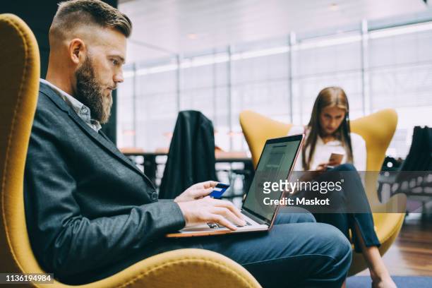 side view of businessman holding credit card while using laptop at airport - airport gate stock pictures, royalty-free photos & images