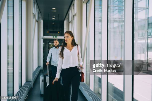 business colleagues pulling luggage while walking in corridor at airport - corporate travel stock-fotos und bilder