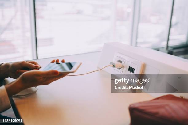 cropped hands of young businesswoman charging smart phone at table while waiting in airport departure area - airport smartphone stock-fotos und bilder