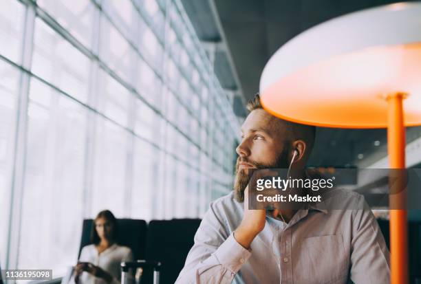 thoughtful businessman looking away while sitting at airport departure area - embarquement photos et images de collection