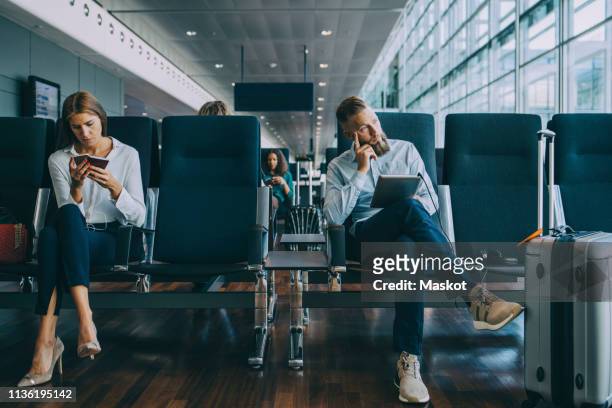thoughtful businessman looking away while sitting by female colleague at waiting area in airport - aspettare foto e immagini stock