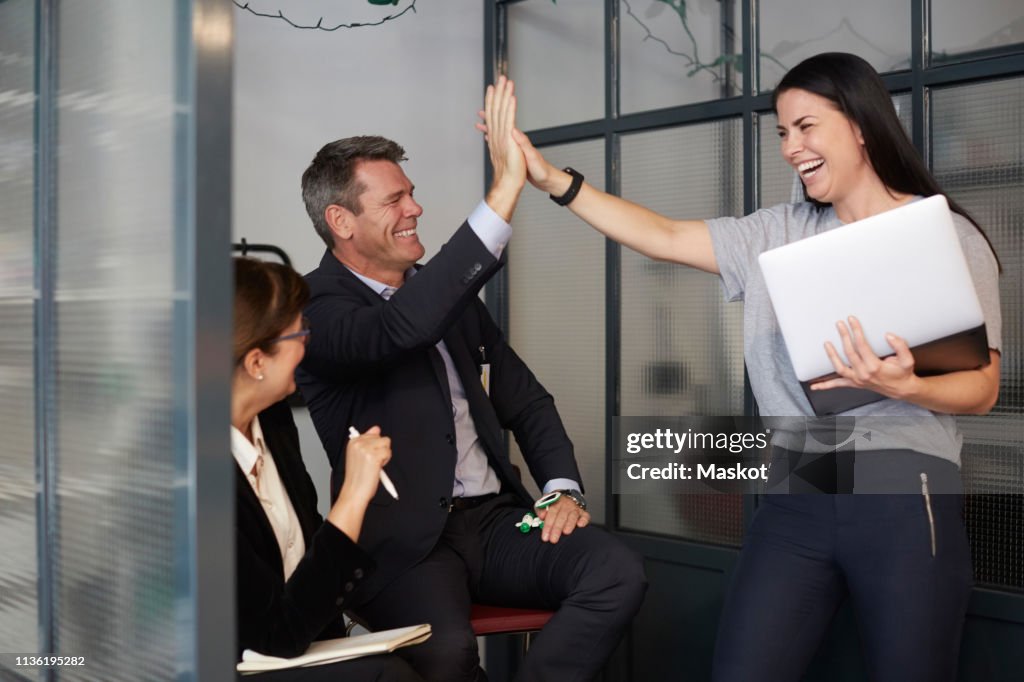 Cheerful creative businesswoman high-fiving with male bank manager during meeting in office