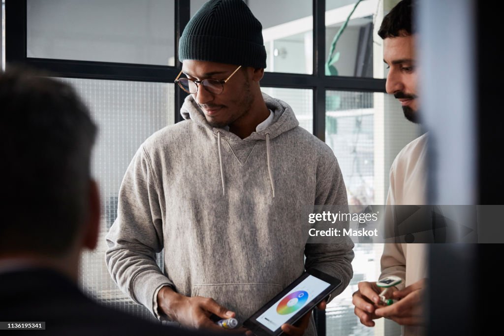 Male entrepreneur holding digital tablet while standing by colleague during meeting in creative office
