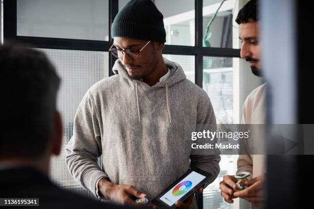 male entrepreneur holding digital tablet while standing by colleague during meeting in creative office - sales pitch stock pictures, royalty-free photos & images