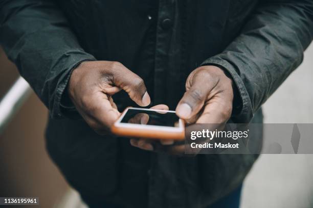 midsection of businessman using smart phone while standing on footbridge in city - black hand holding phone stock-fotos und bilder