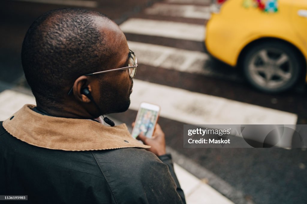 Rear view of businessman using mobile phone while crossing road in city