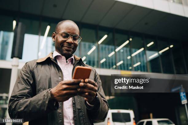 low angle view of businessman using smart phone while standing against building in city - receding hairline stock pictures, royalty-free photos & images