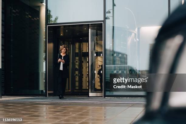 full length of businesswoman using smart phone while leaving from office - leaving stock-fotos und bilder