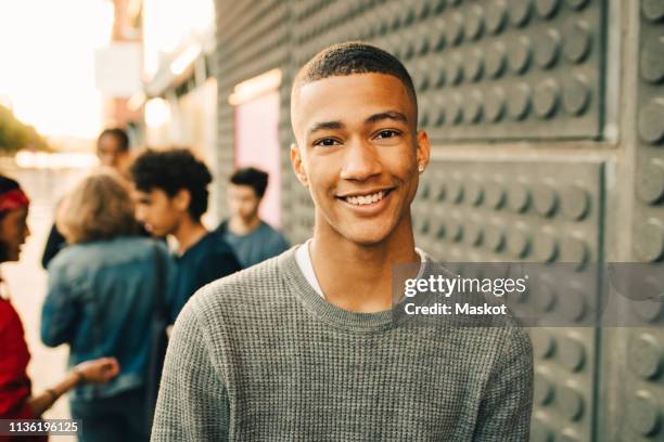 portrait of smiling teenage boy with friends standing in background on street - arab man smiling stock-fotos und bilder