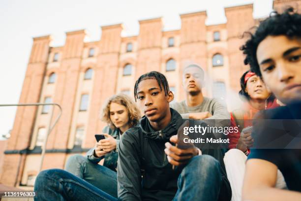 low angle view of male friends sitting in city - serious teenager boy stock-fotos und bilder