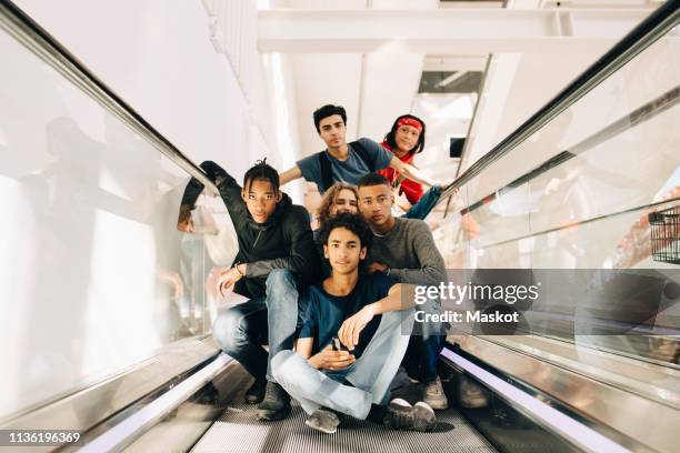 portrait of confident male friends on moving walkway in shopping mall - vorderasiatische abstammung stock-fotos und bilder