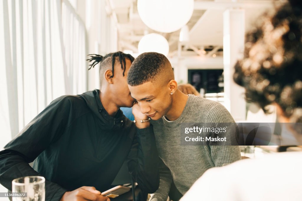Teenage boy whispering into male friend's ear in restaurant